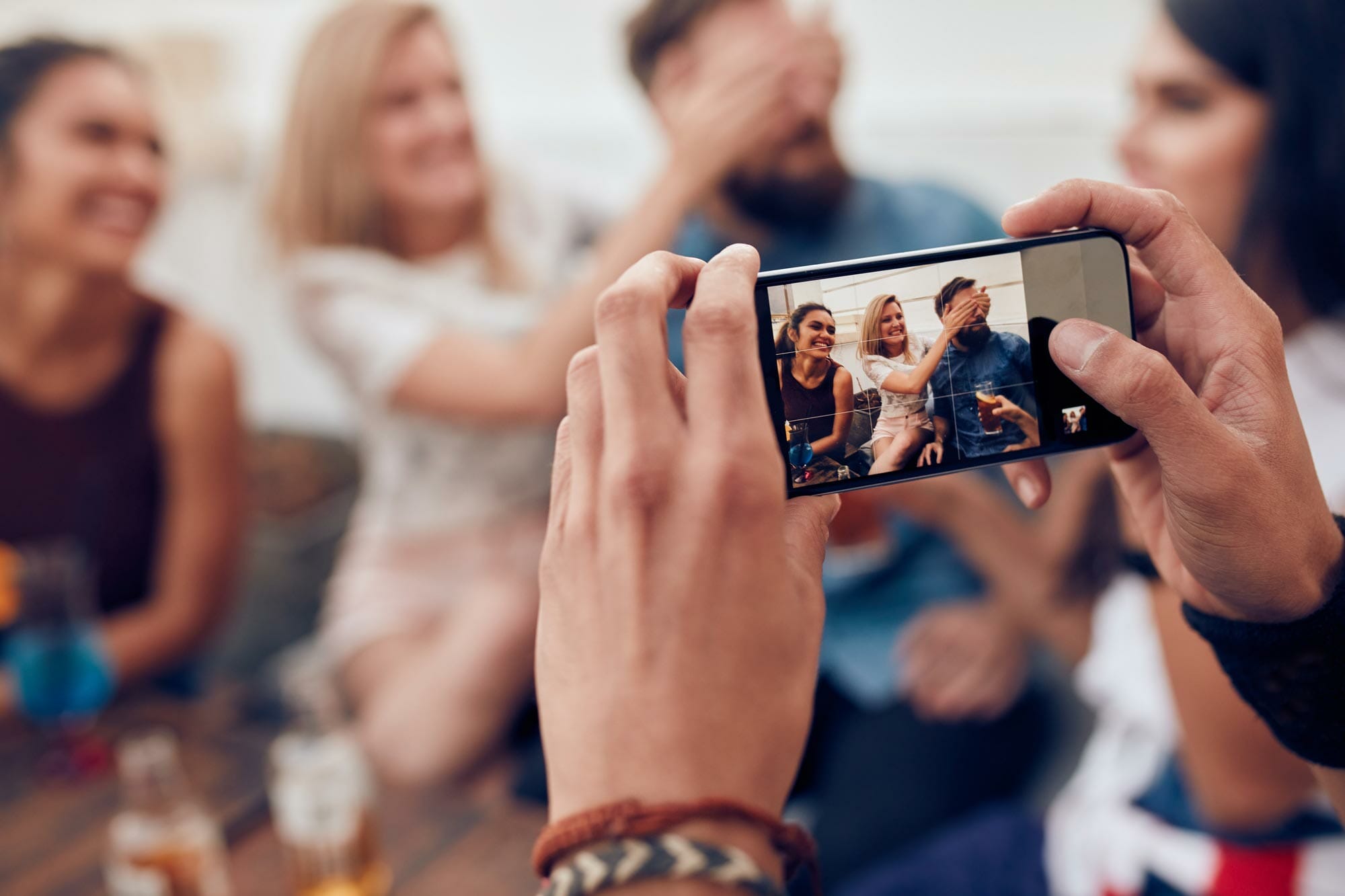 man holding a phone to photograph a group of friends at a party.